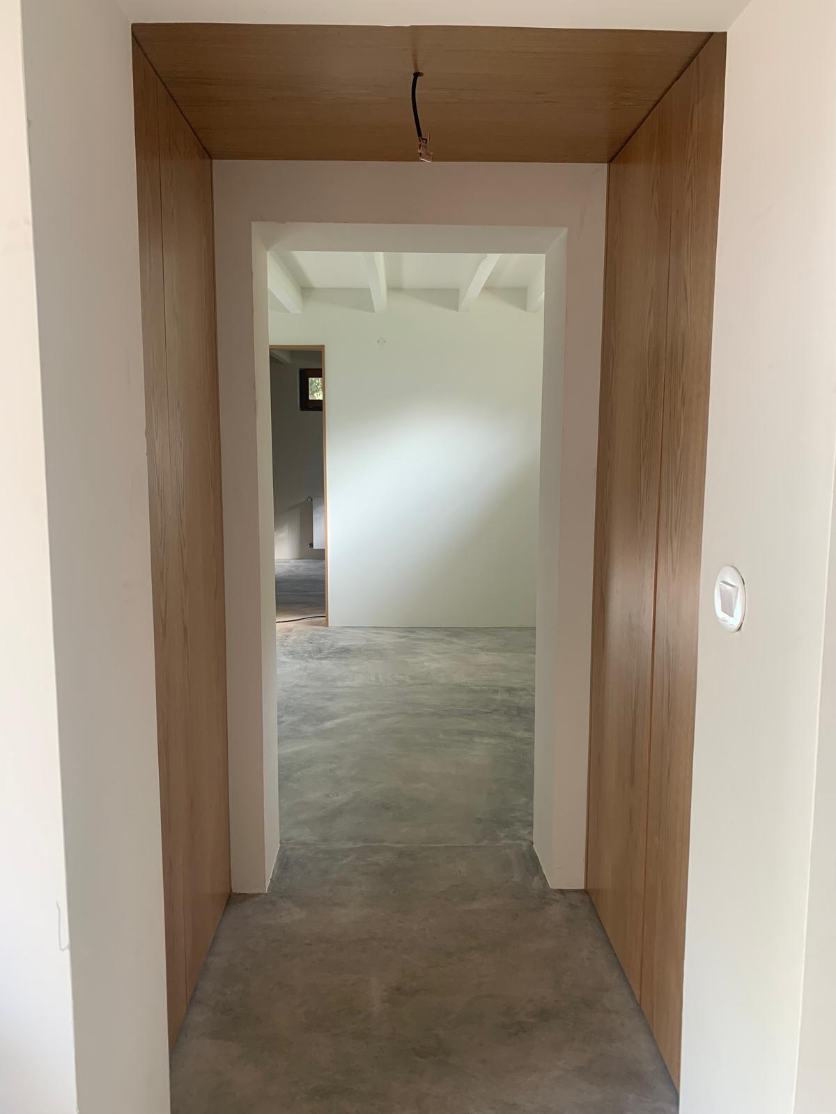 Hallway lined in oak panelling opening onto a room with polished concrete floor