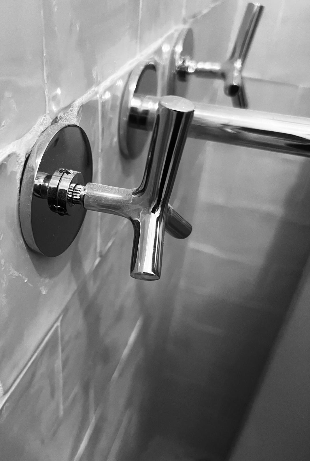 Black and white close-up of a crosshead chrome bath tap on marble tiling